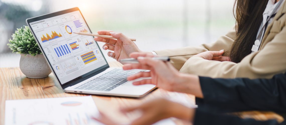 Two professional analyzing financial data graphs, charts on laptop display at a modern workspace. Financial analysis or business evaluation concept